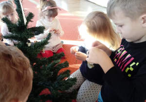 Dzieci wieszają ozdoby świąteczne na choince